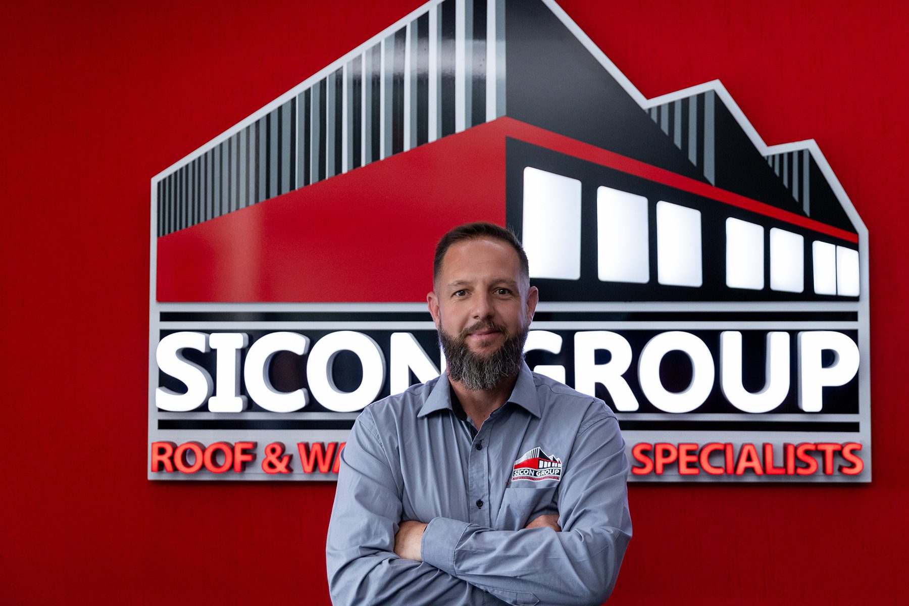 Professional photo of Anton Barnard standing confidently in front of the Sicon Group logo wall, dressed in company attire.