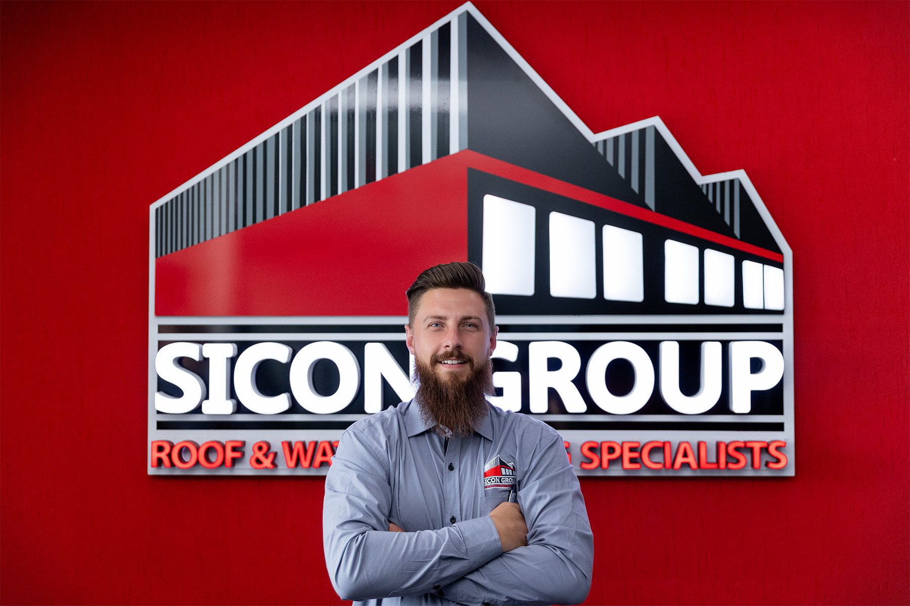 Confident photo of Schalk Jooste in front of the Sicon Group logo wall, representing the company’s expert roofing and waterproofing solutions.