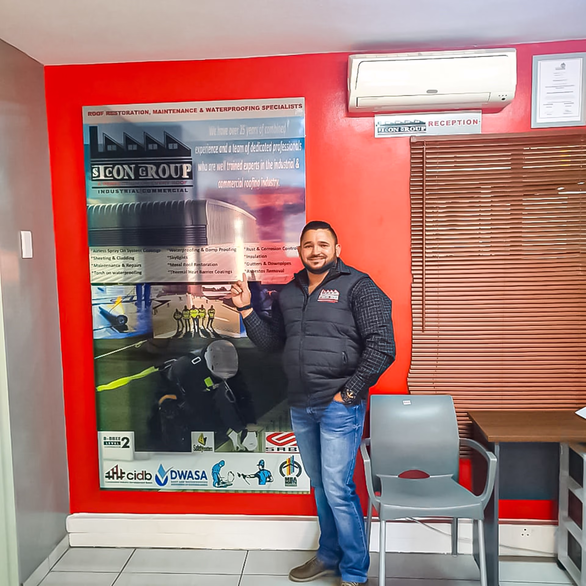 Sicon CEO pointing to a wall display banner showing projects and services