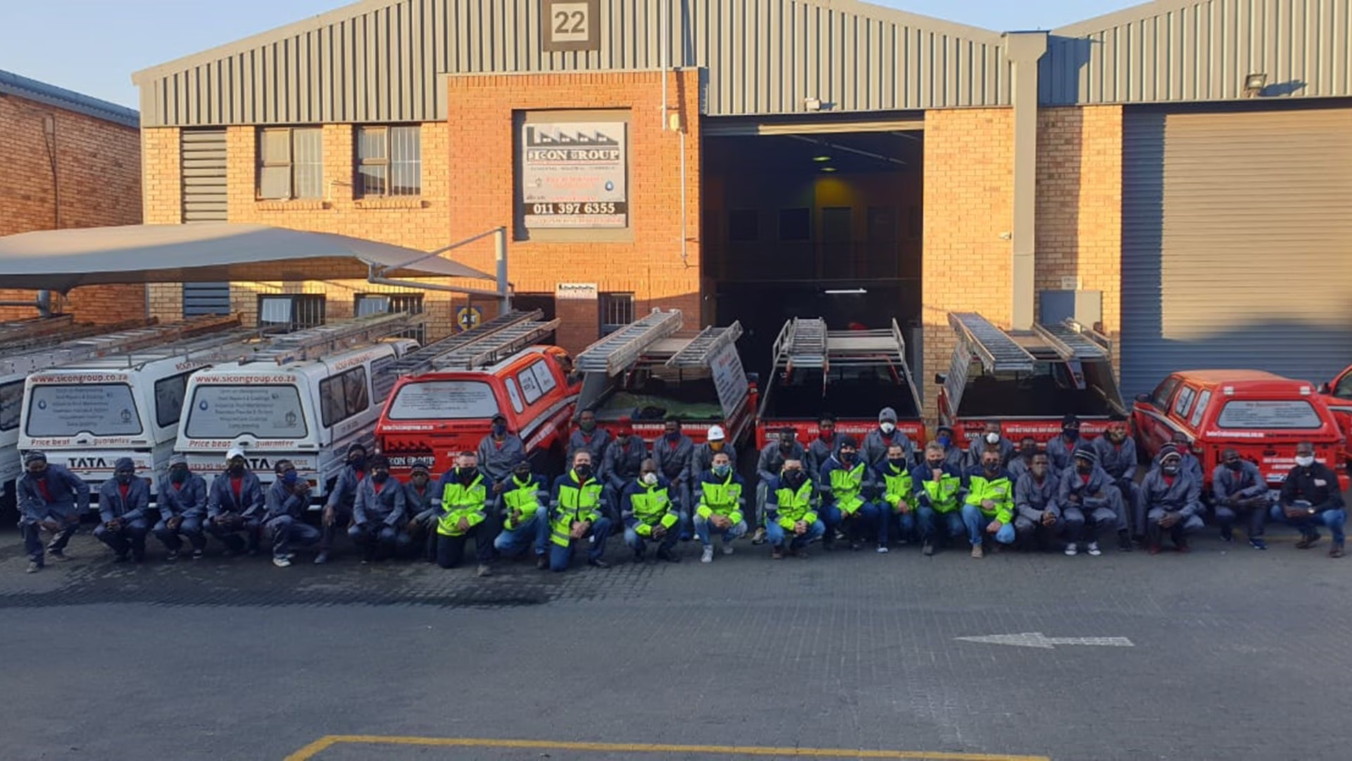 Large group of Sicon staff in uniform posing in front of company vehicles at one of the branches