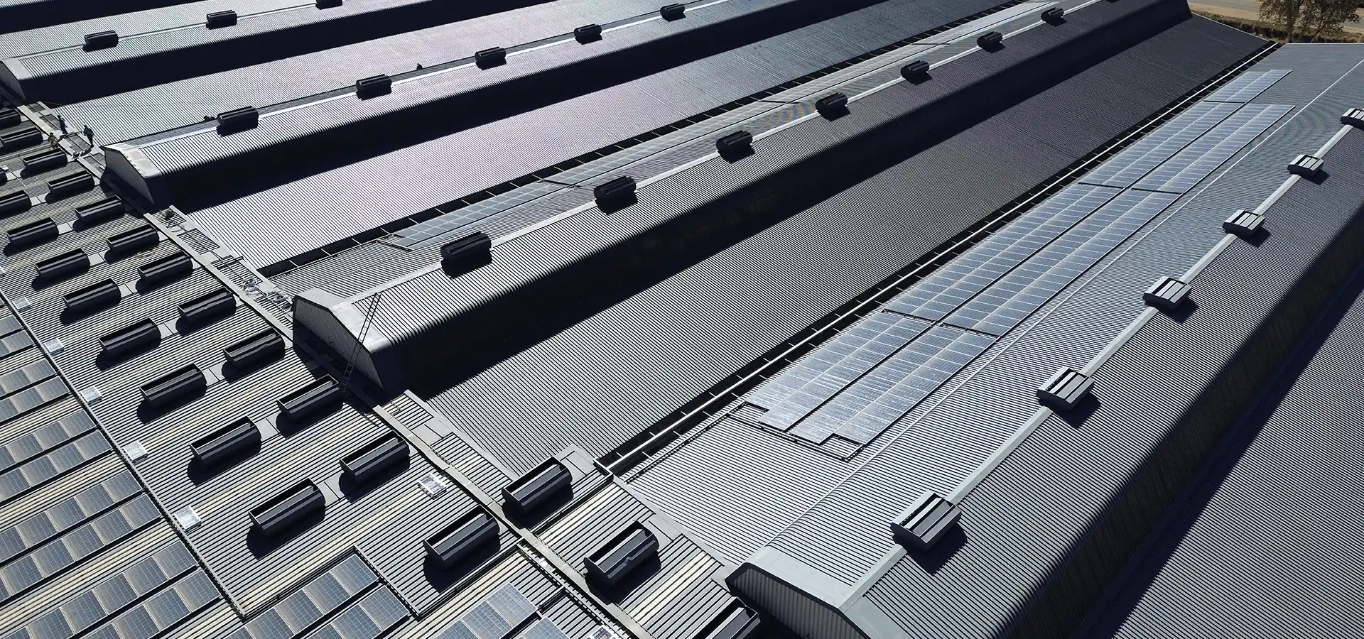 Aerial view of a vast industrial corrugated metal roof featuring solar panels and vents indicating complex Roof Repairs done by Sicon Group in Johannesburg